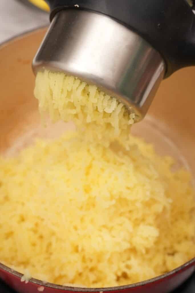 Ricing boiled potatoes into a pot.