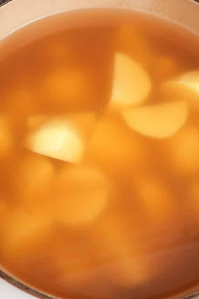 Simmering potatoes in chicken broth in a pot.