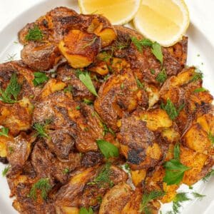 Crispy smashed potatoes on a plate with lemon wedges.