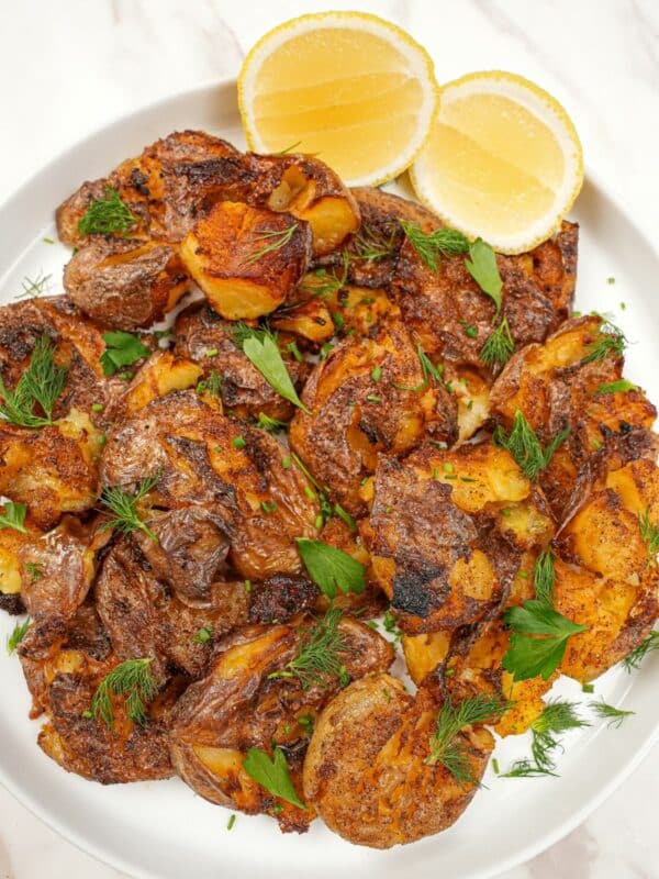 Crispy smashed potatoes on a plate with lemon wedges.