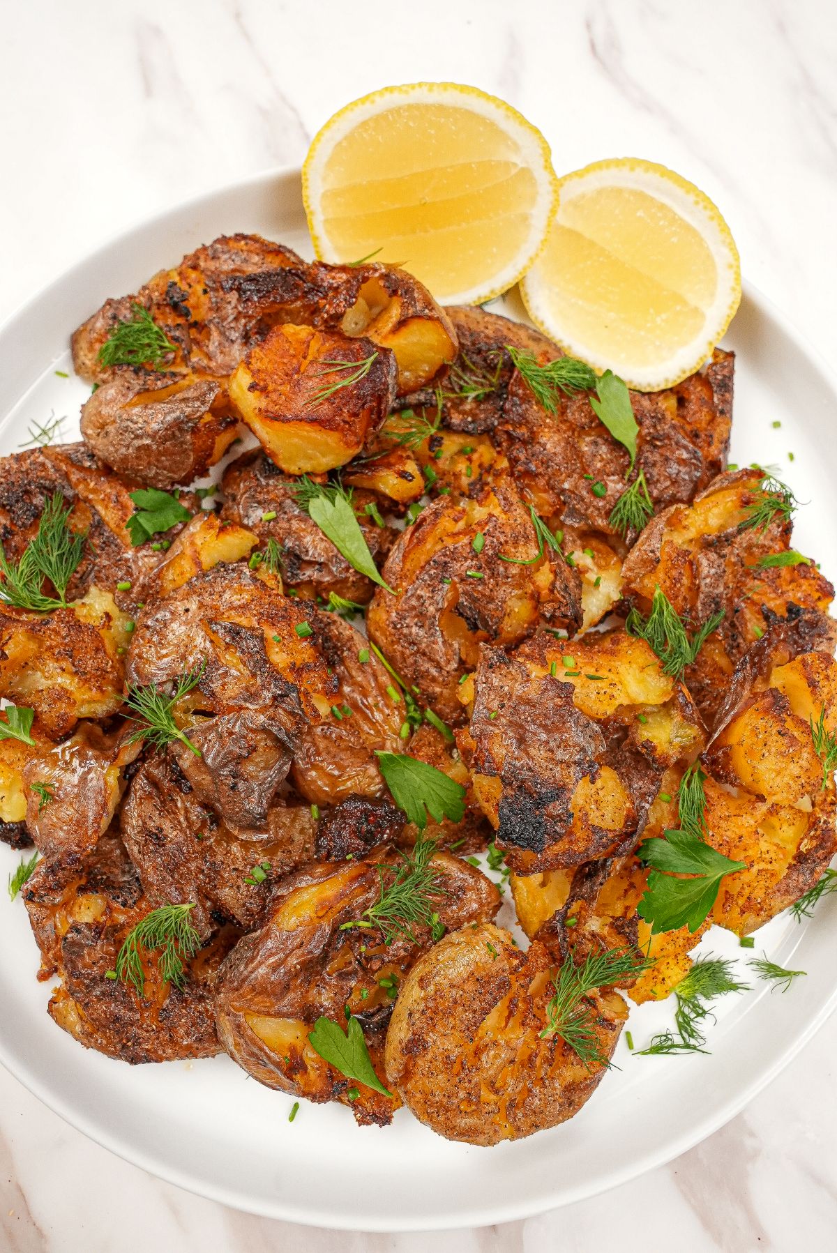 Crispy smashed potatoes on a plate with lemon wedges.