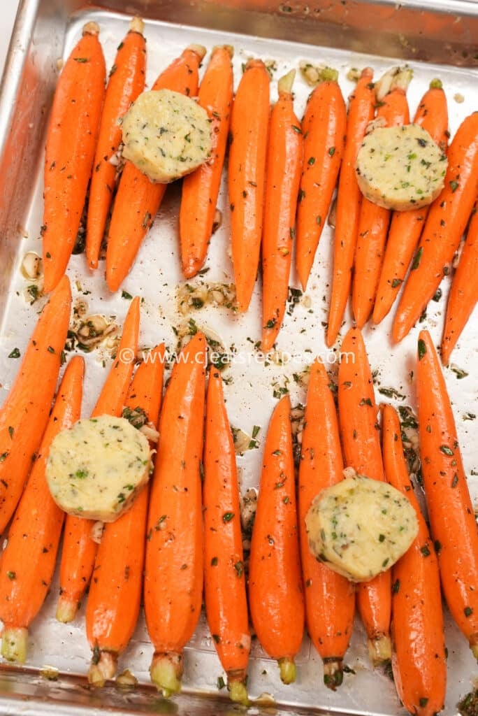 Herb butter on the carrots in a baking tray.