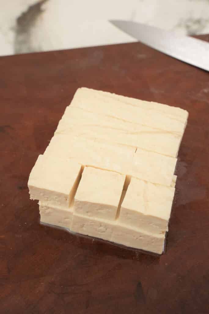 Tofu cut into cubes on a cutting board.