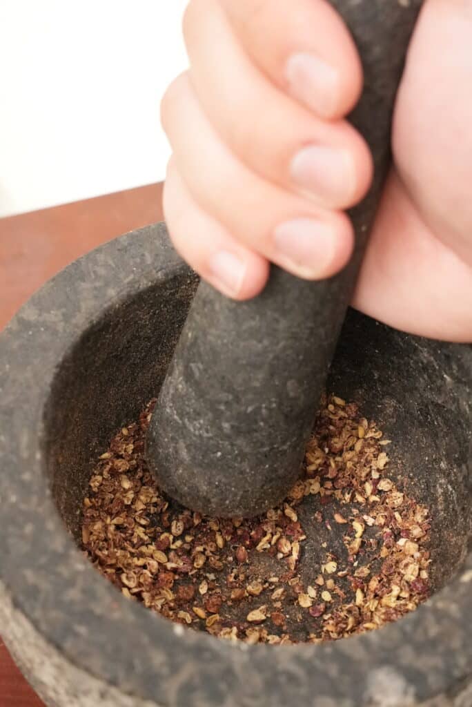 Grinding szechuan peppercorns with a mortar and pestle.