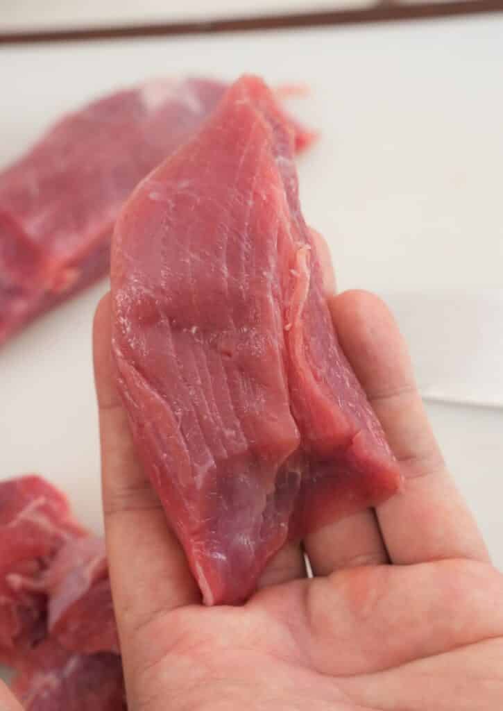 A hand holding a piece of steak to show the muscle fibers.