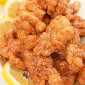 A plate of Chinese Lemon Chicken on a plate with lemon slices and rice.