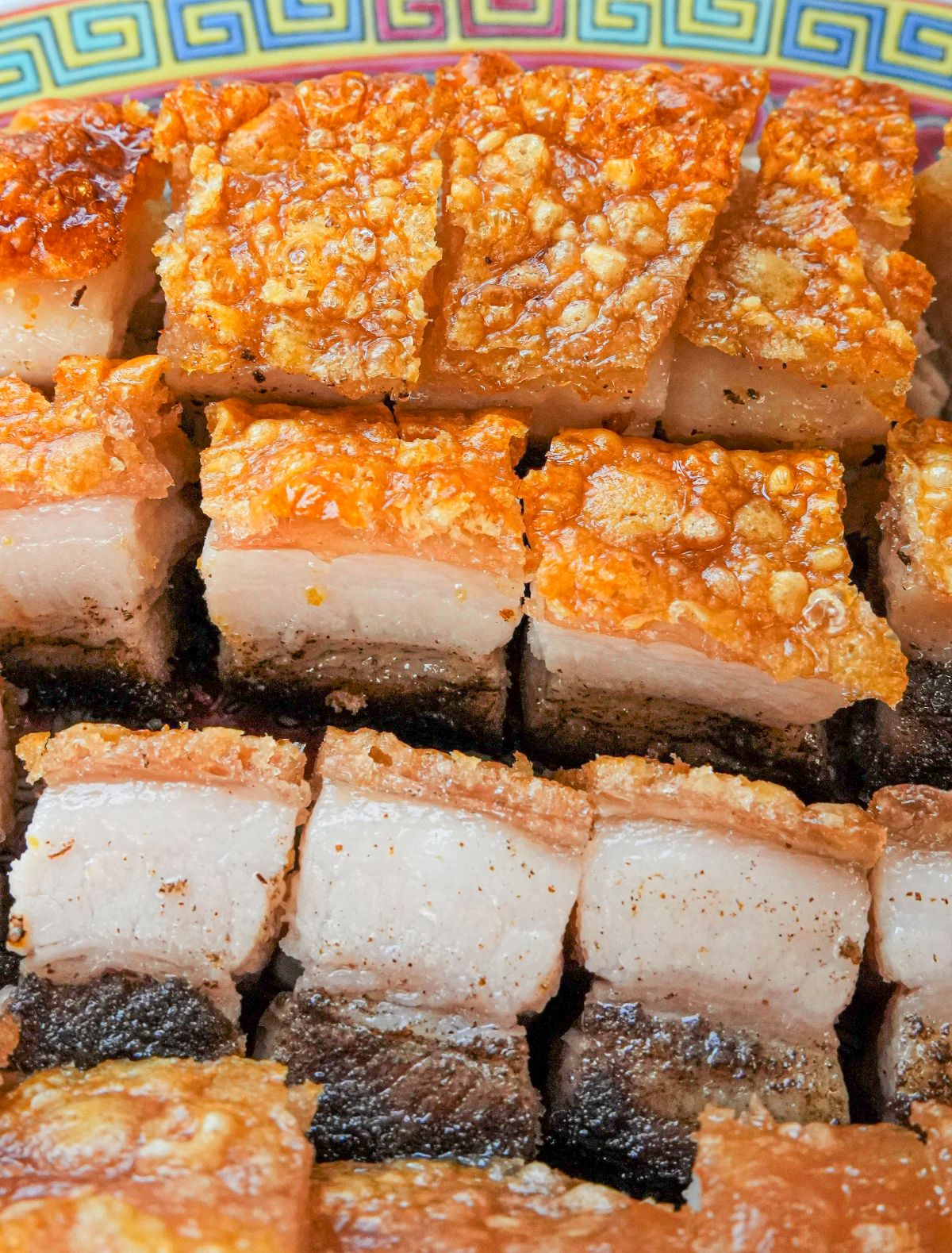 A Chinese Crispy Pork Belly (Siu Yuk) cut into pieces on a decorative Chinese plate.