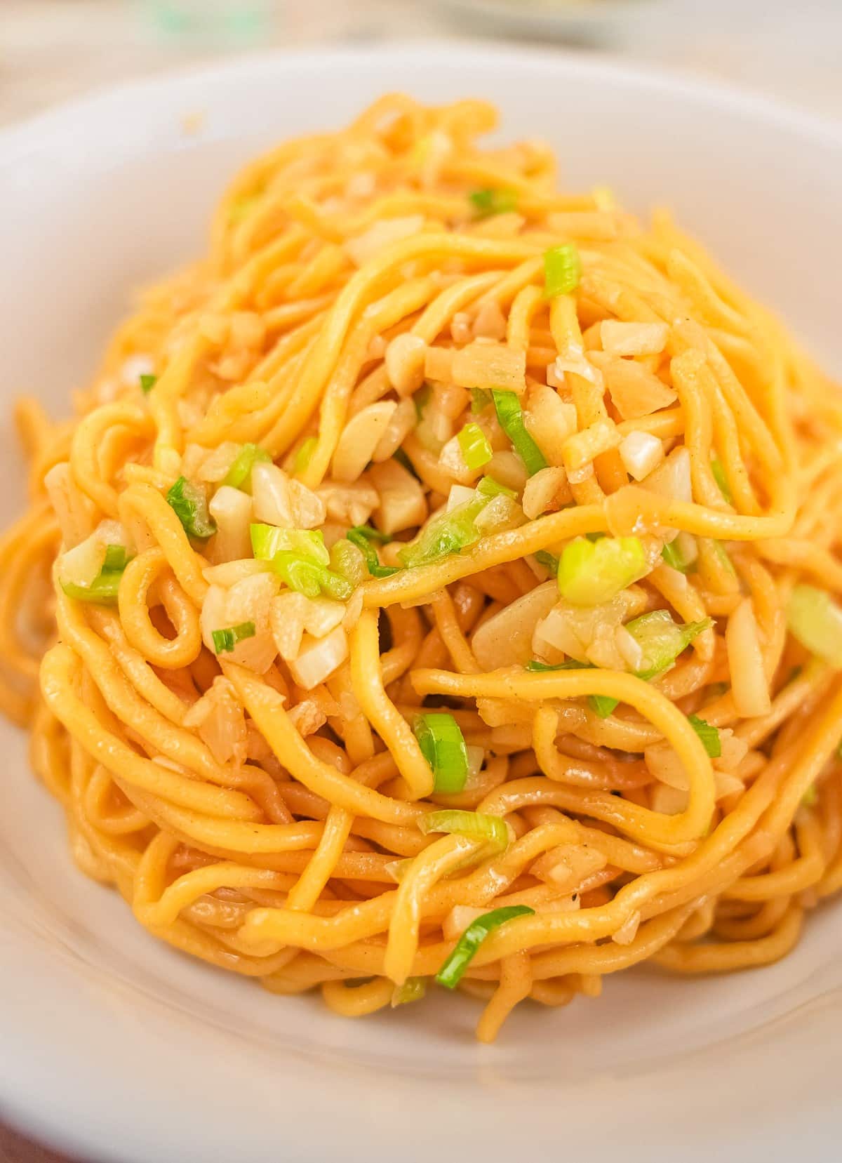 A bowl of asian garlic noodles with fresh garlic and scallions.