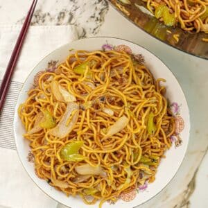 Copycat Panda Express Chow Mein in a bowl next to chopsticks and a wok with more chow mein.