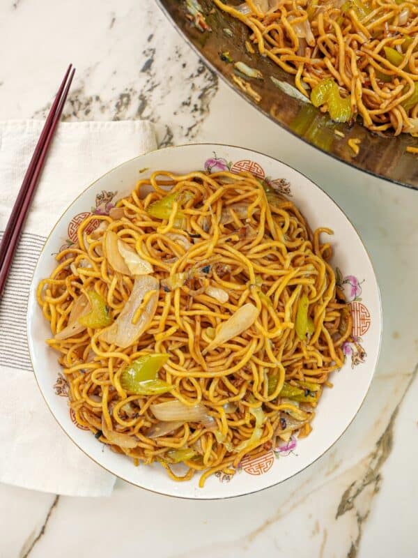 Copycat Panda Express Chow Mein in a bowl next to chopsticks and a wok with more chow mein.