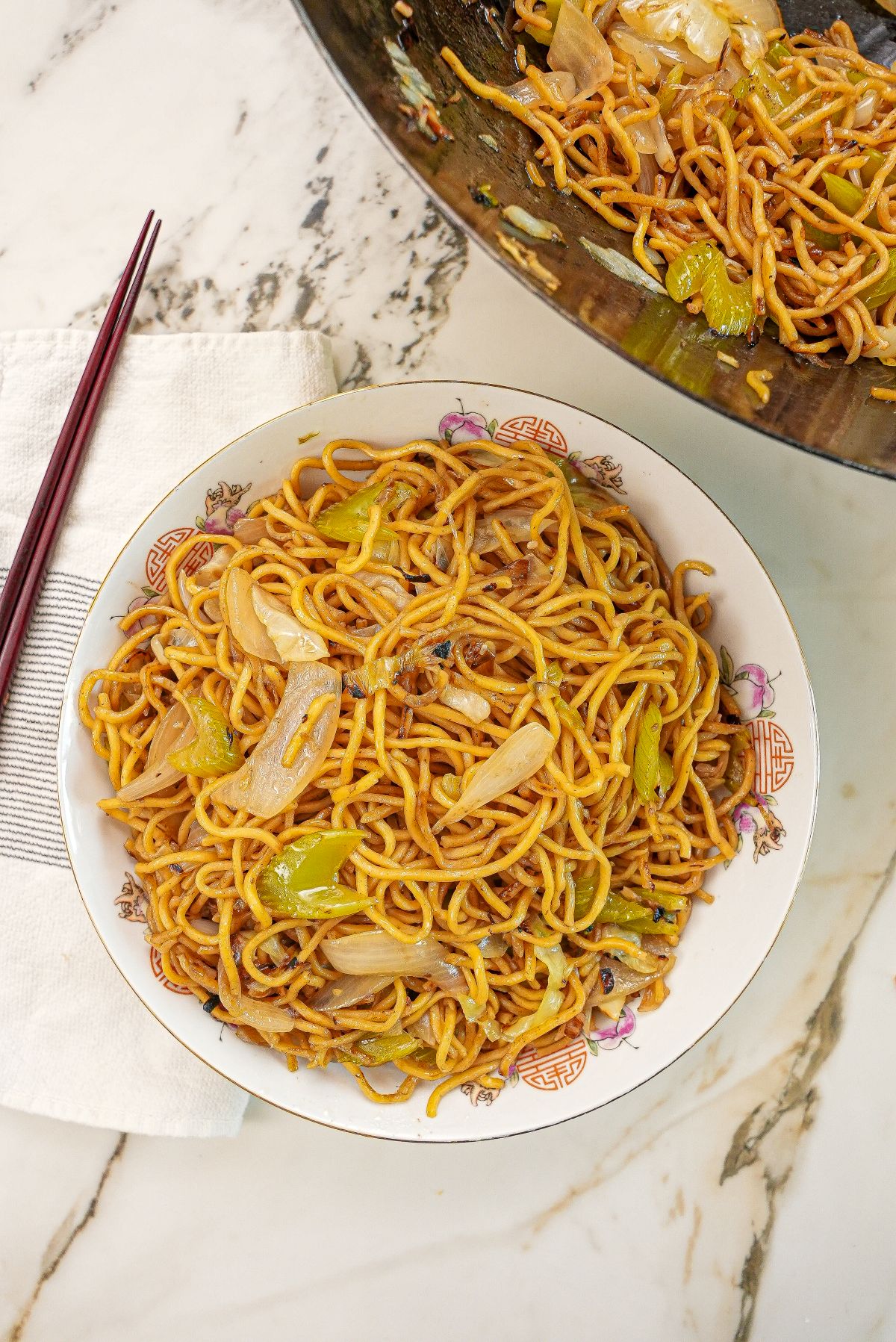 Copycat Panda Express Chow Mein in a bowl next to chopsticks and a wok with more chow mein.