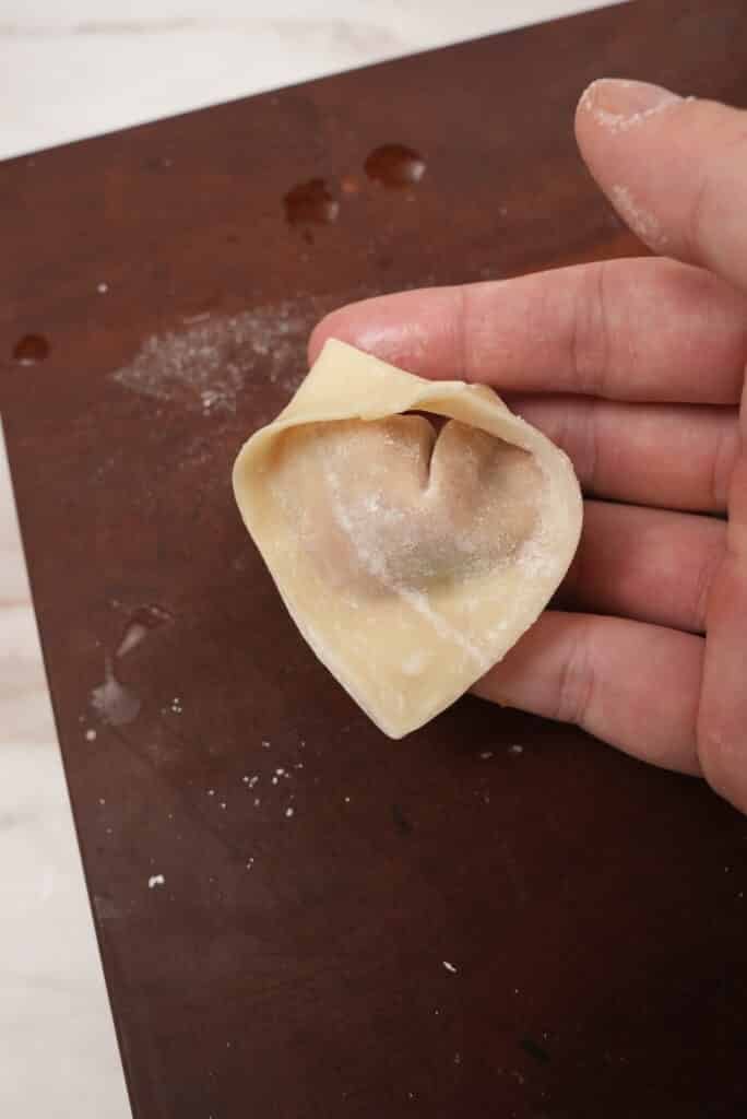 A folded chicken wonton on a cutting board.