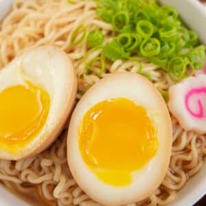 A ramen egg cut in half on top of a bowl of ramen noodles with scallions and fish cake.