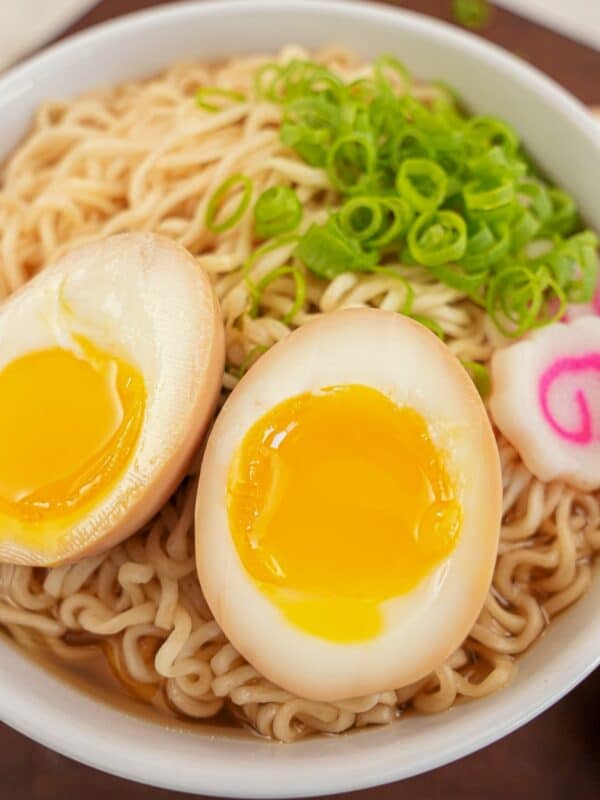 A ramen egg cut in half on top of a bowl of ramen noodles with scallions and fish cake.
