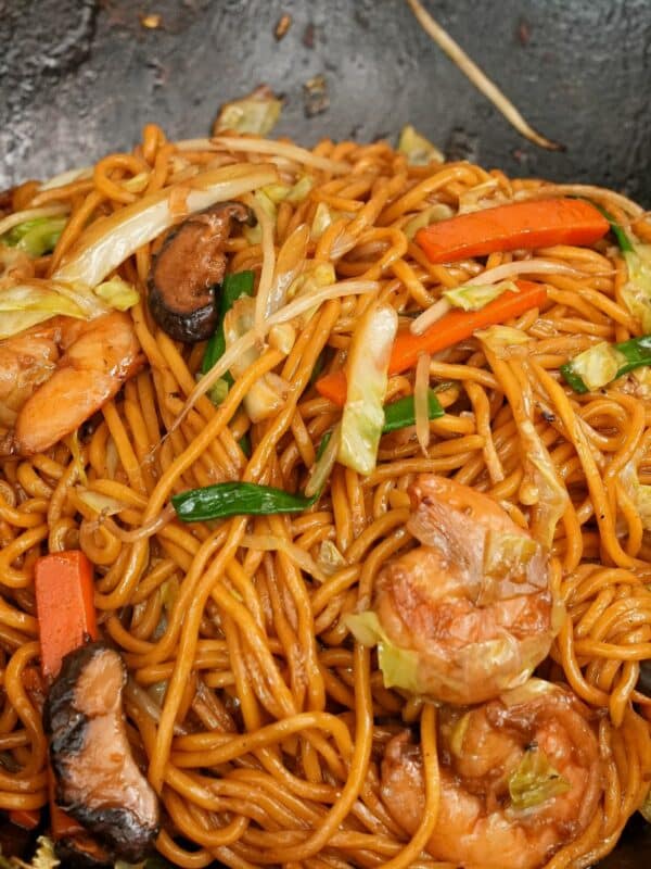 Shrimp Lo Mein cooked in a wok with shrimp, noodles, mushrooms, cabbage, carrots, scallions, and lo mein sauce.