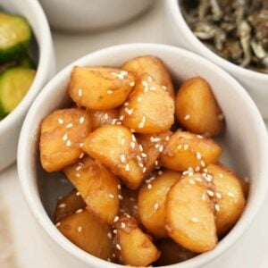 Korean braised potatoes in a bowl next to other bowls of banchan or Korean side dishes.
