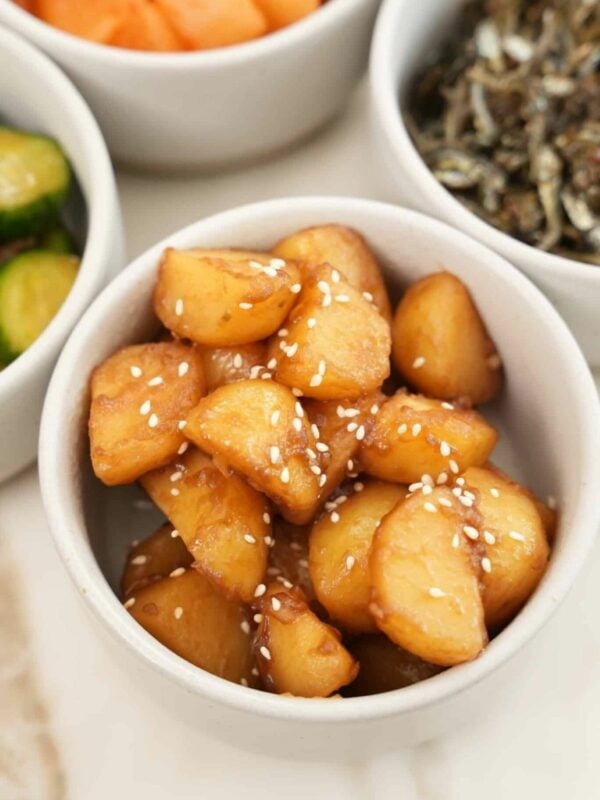 Korean braised potatoes in a bowl next to other bowls of banchan or Korean side dishes.
