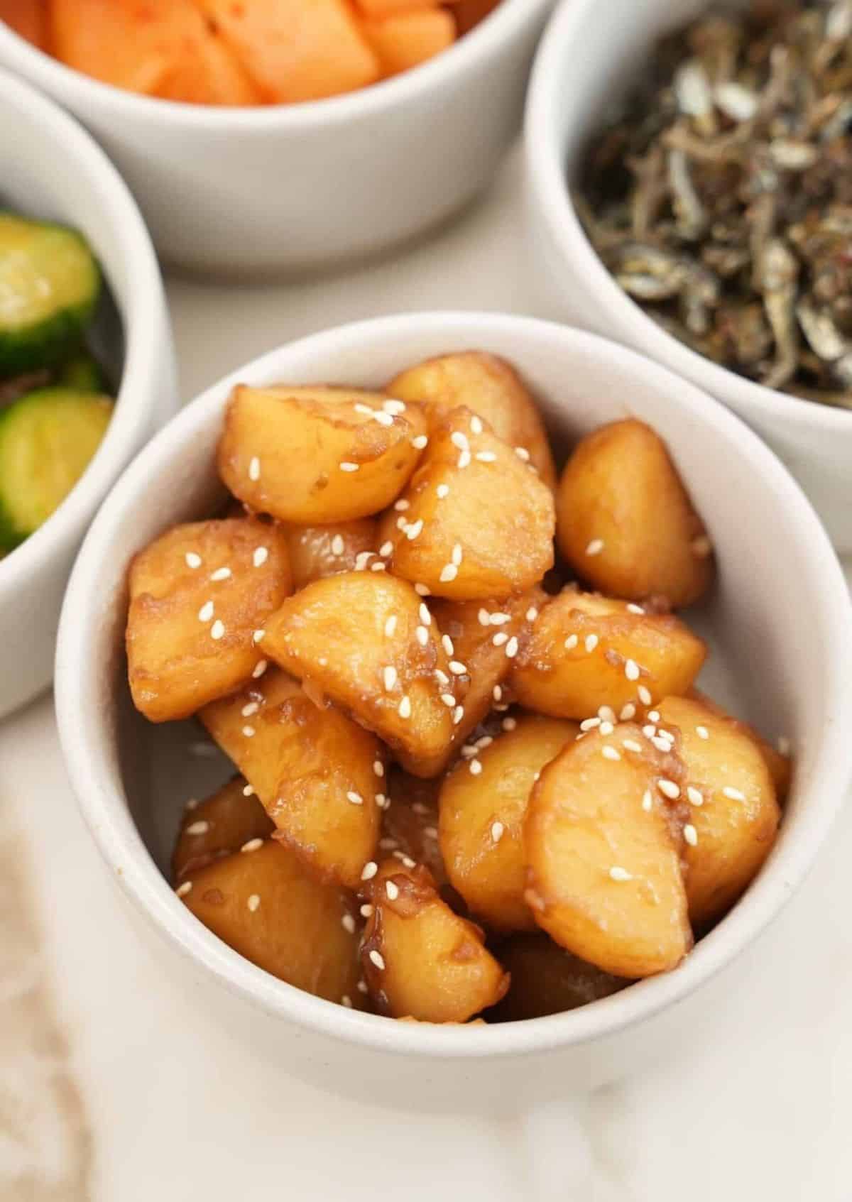 Korean braised potatoes in a bowl next to other bowls of banchan or Korean side dishes.