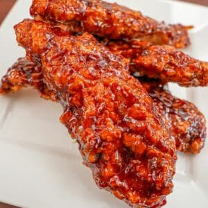 Korean Fried Chicken Tenders on a plate tossed in a spicy gochujang sauce.