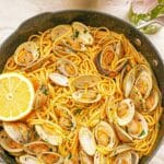 A pan full of cooked Linguine with Clams with a lemon wedge.
