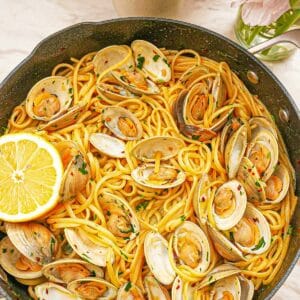 A pan full of cooked Linguine with Clams with a lemon wedge.