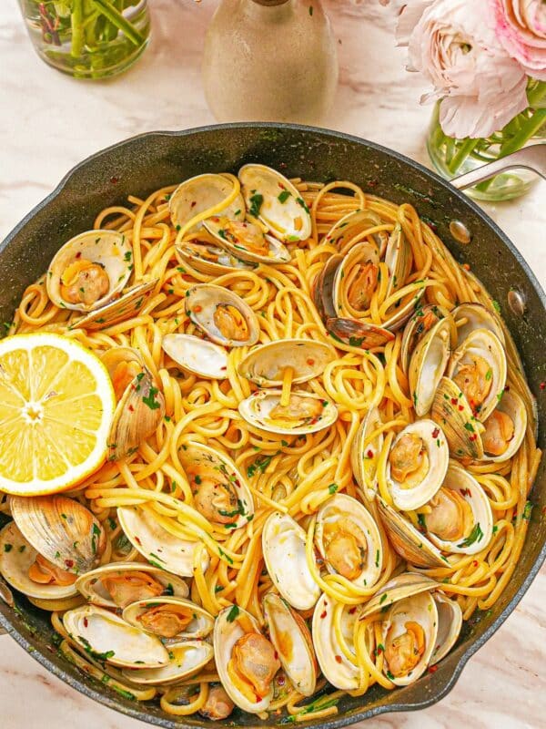 A pan full of cooked Linguine with Clams with a lemon wedge.