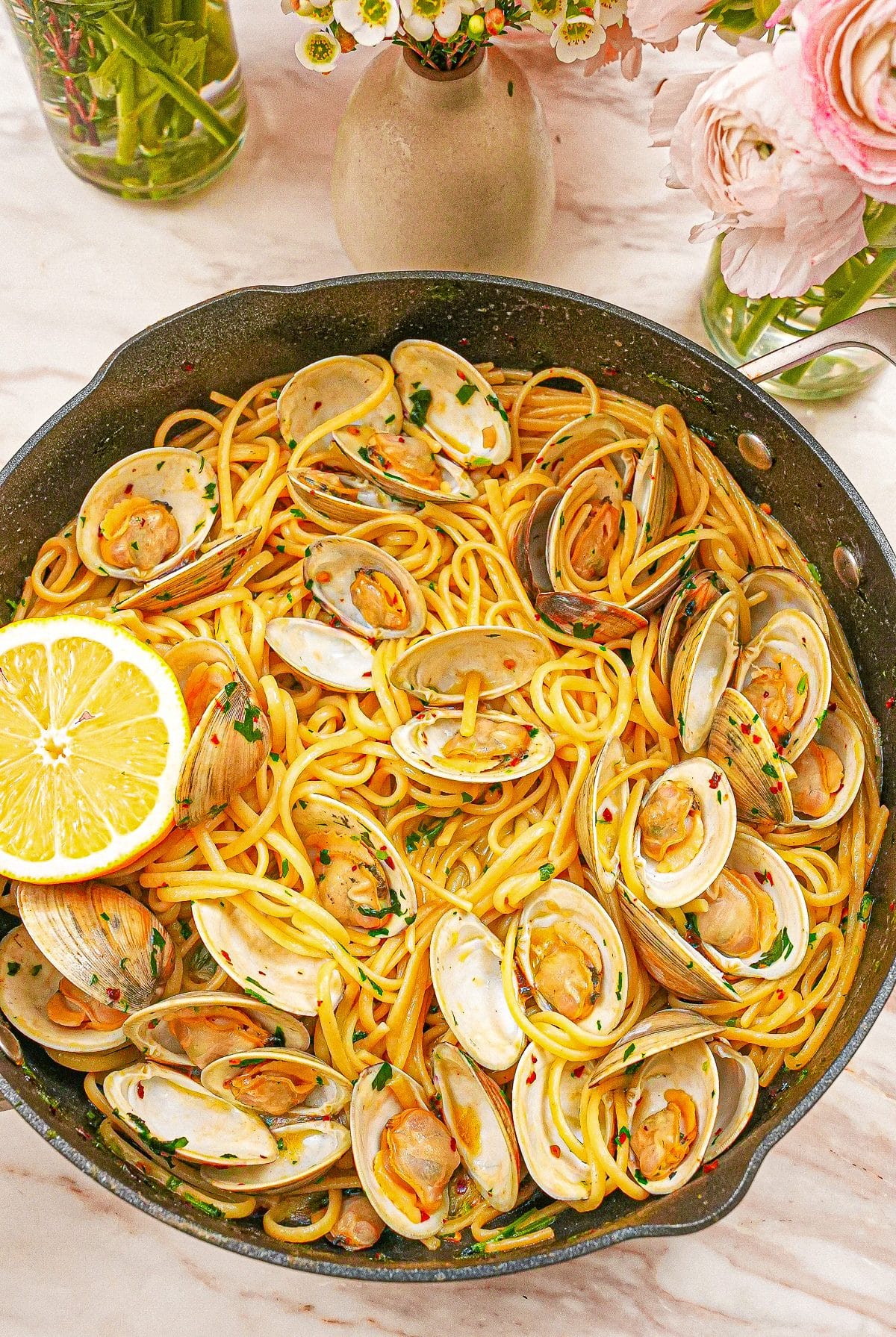 A pan full of cooked Linguine with Clams with a lemon wedge.