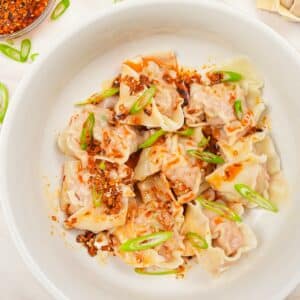 A bowl of chinese pork and shrimp wontons with chili oil and scallions.