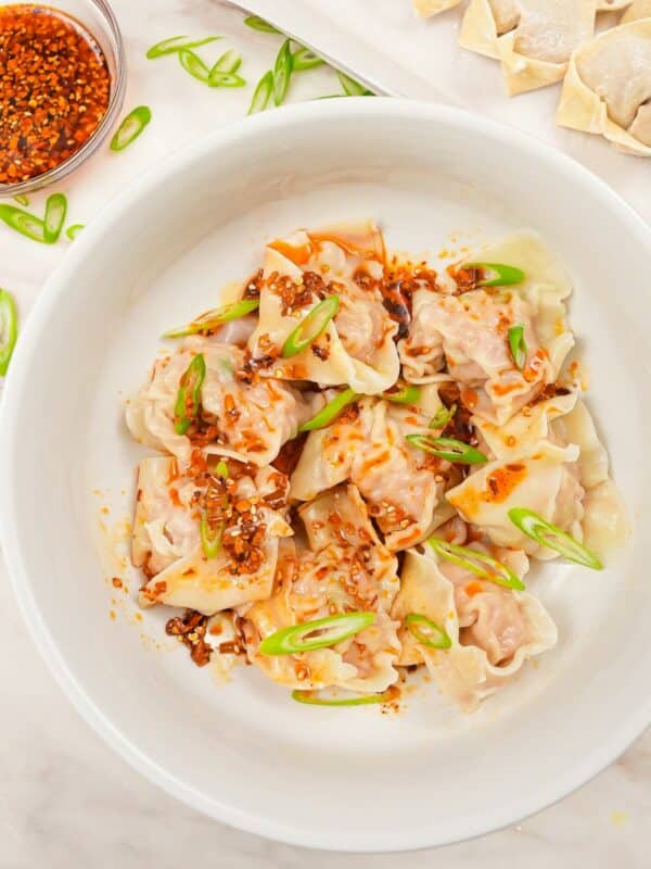 A bowl of chinese pork and shrimp wontons with chili oil and scallions.