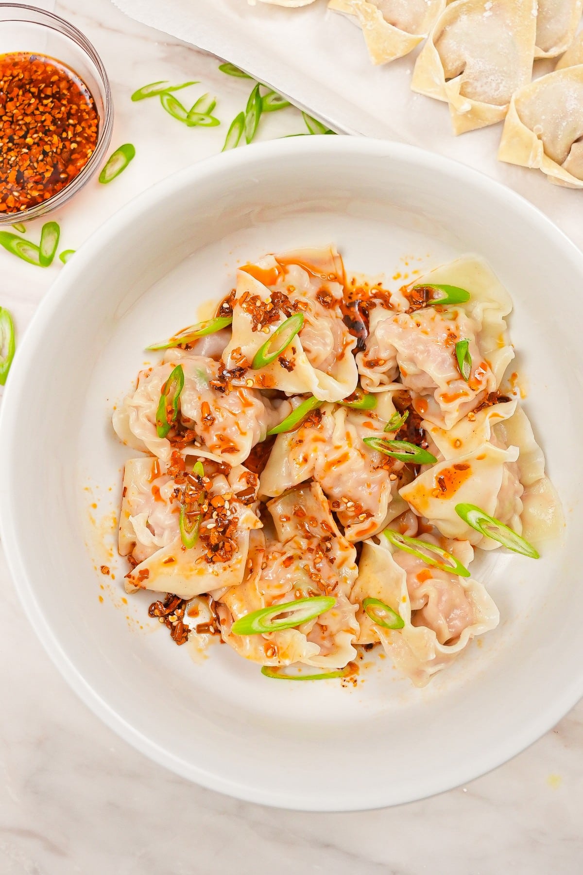 A bowl of chinese pork and shrimp wontons with chili oil and scallions.