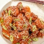 Sesame chicken in a bowl with white rice and scallions.
