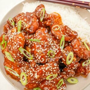 Sesame chicken in a bowl with white rice and scallions.