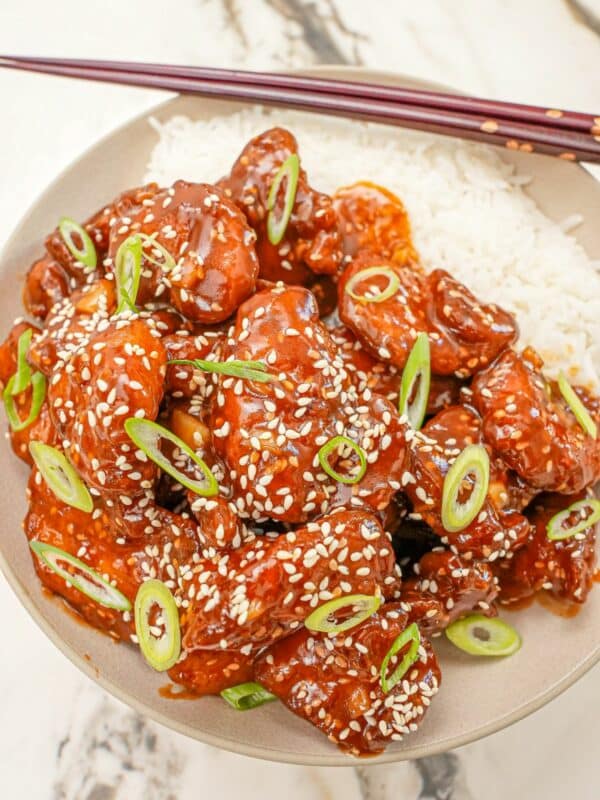 Sesame chicken in a bowl with white rice and scallions.
