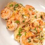 Shrimp scampi pasta plated in a white bowl with shrimp, chili flakes, and parsley.