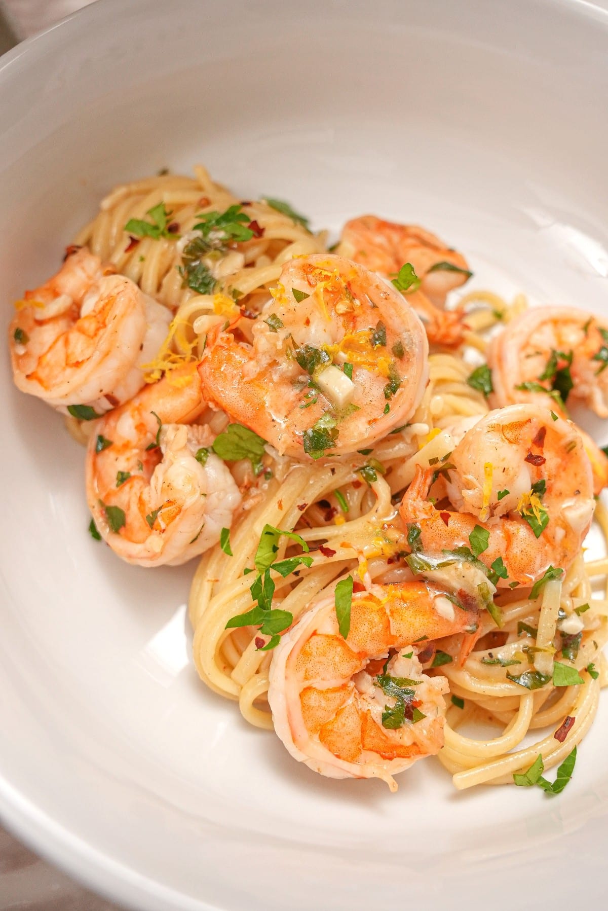 Shrimp scampi pasta plated in a white bowl with shrimp, chili flakes, and parsley.