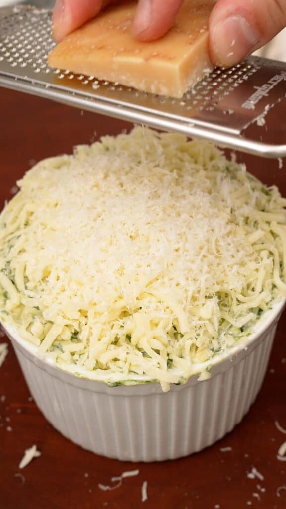 Grating parmesan cheese over spinach artichoke dip