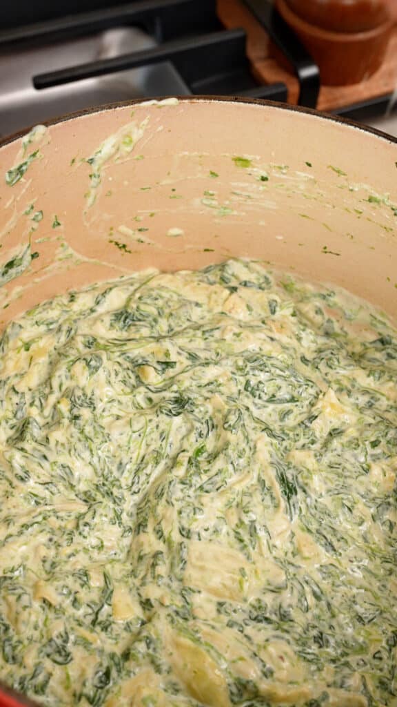 Mixing spinach, artichoke, cheese, and sour cream in a pot