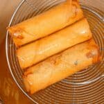 Crispy egg rolls in a strainer over hot oil.