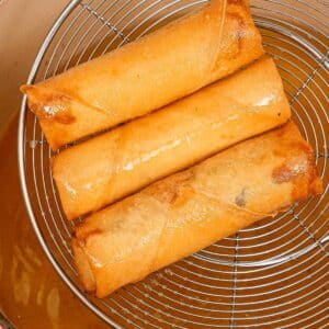 Crispy egg rolls in a strainer over hot oil.