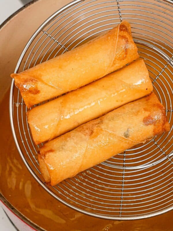 Crispy egg rolls in a strainer over hot oil.