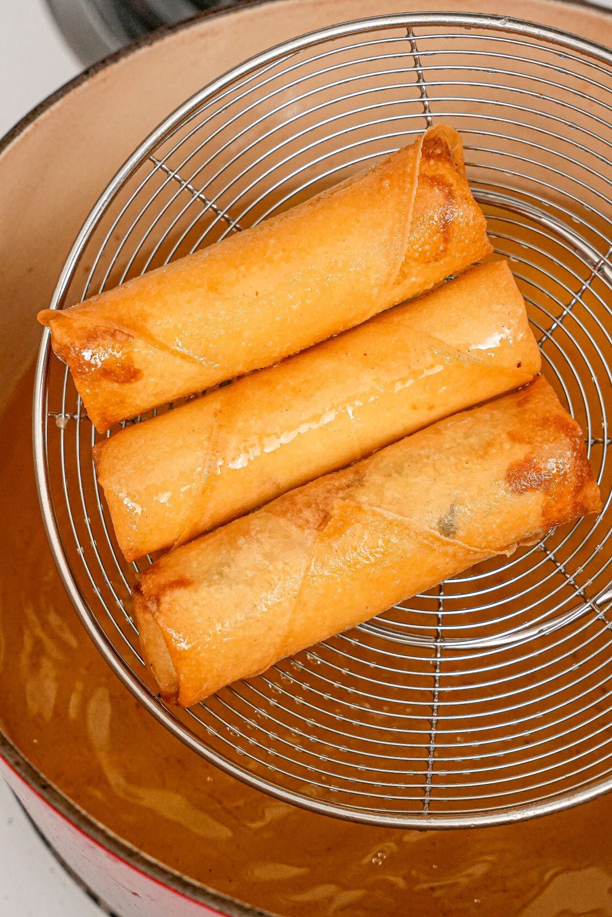 Crispy egg rolls in a strainer over hot oil.