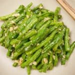A plate of copycat Din Tai Fung Green Beans in a grey bowl with chopsticks.