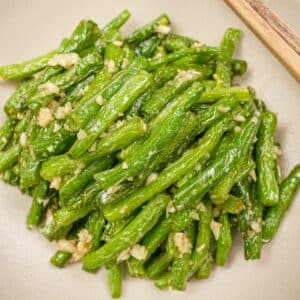 A plate of copycat Din Tai Fung Green Beans in a grey bowl with chopsticks.