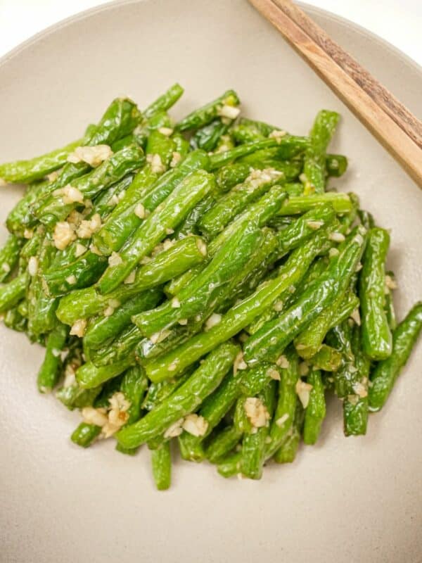 A plate of copycat Din Tai Fung Green Beans in a grey bowl with chopsticks.