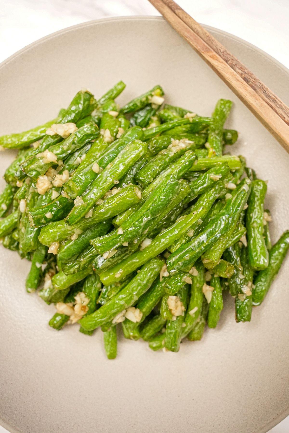 A plate of copycat Din Tai Fung Green Beans in a grey bowl with chopsticks.