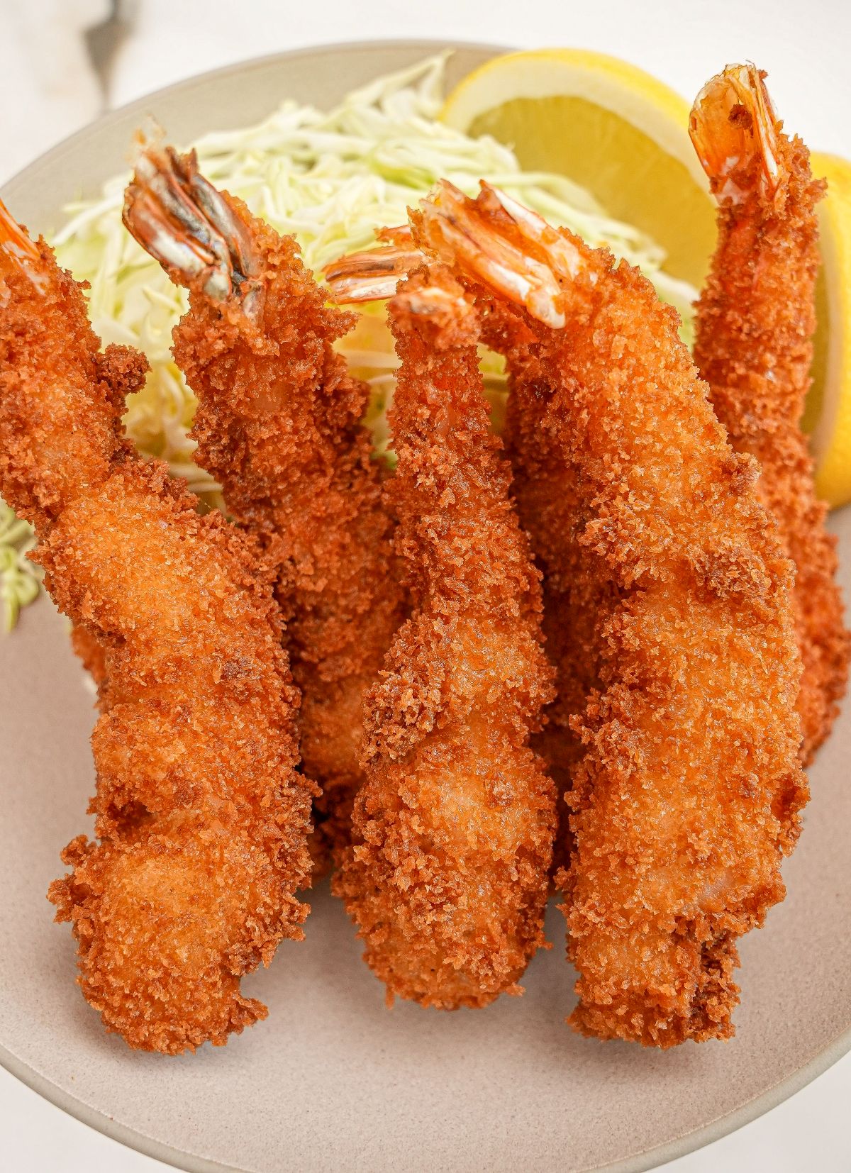 A bowl of fried panko shrimp with shredded cabbage and lemon.