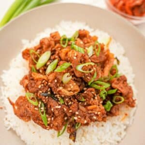 Korean spicy pork bulgogi on top of white rice in a bowl next to a small bowl of kimchi.