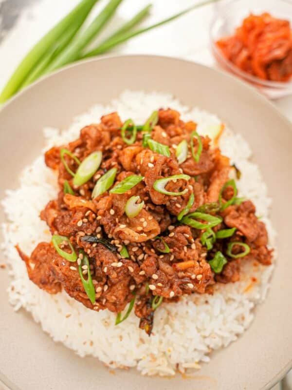 Korean spicy pork bulgogi on top of white rice in a bowl next to a small bowl of kimchi.