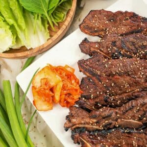 A plate of Korean marinated short ribs (Galbi) on a plate with kimchi and lettuce.