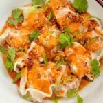Wontons with Spicy Peanut Sauce in a bowl with cilantro and chopsticks.